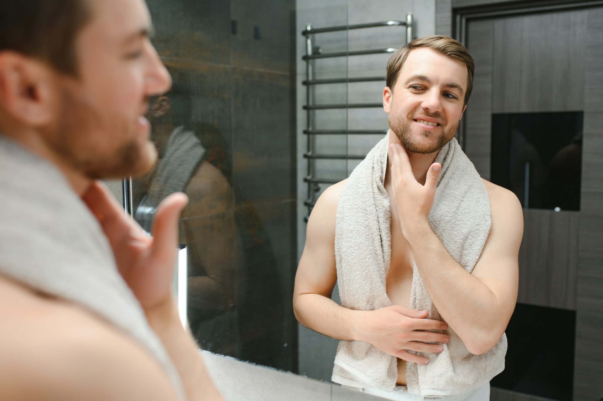 Handsome shirtless man looking in the mirror in the bathroom